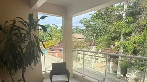 Ein Balkon mit Korbmöbeln, einem Glastisch und einer großen Pflanze.