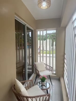Un balcón con sillas de mimbre, una mesa de vidrio y una planta en maceta.