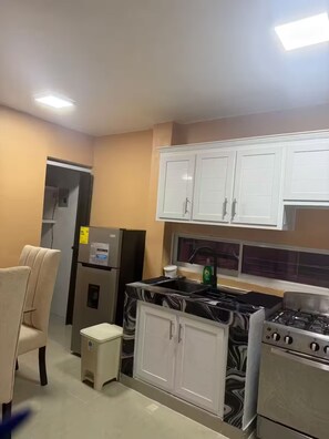 Una cocina con armarios blancos, un refrigerador, una estufa y un lavamanos.
