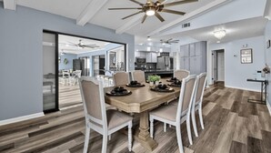 A dining area with a wooden table, white chairs, and ceiling fans. - Footprints In The Sand | 3BR Private Pool Home | Near Palm Coast and Flagler Beaches (Palm Coast)