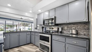 A modern kitchen with grey cabinets, a stone backsplash, and stainless steel appliances. - Footprints In The Sand | 3BR Private Pool Home | Near Palm Coast and Flagler Beaches (Palm Coast)