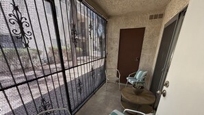 Un petit balcon avec des balustrades en métal, une chaise, un banc rembourré et une porte.