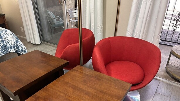 Une pièce avec une table en bois et deux chaises rouges, une porte-fenêtre coulissante et une vue sur l’extérieur.