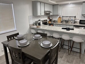 A modern kitchen with grey cabinets, a granite countertop, and a dining area with a table set for four. - Jamming Jericho 2 bedrooms (Las Vegas)