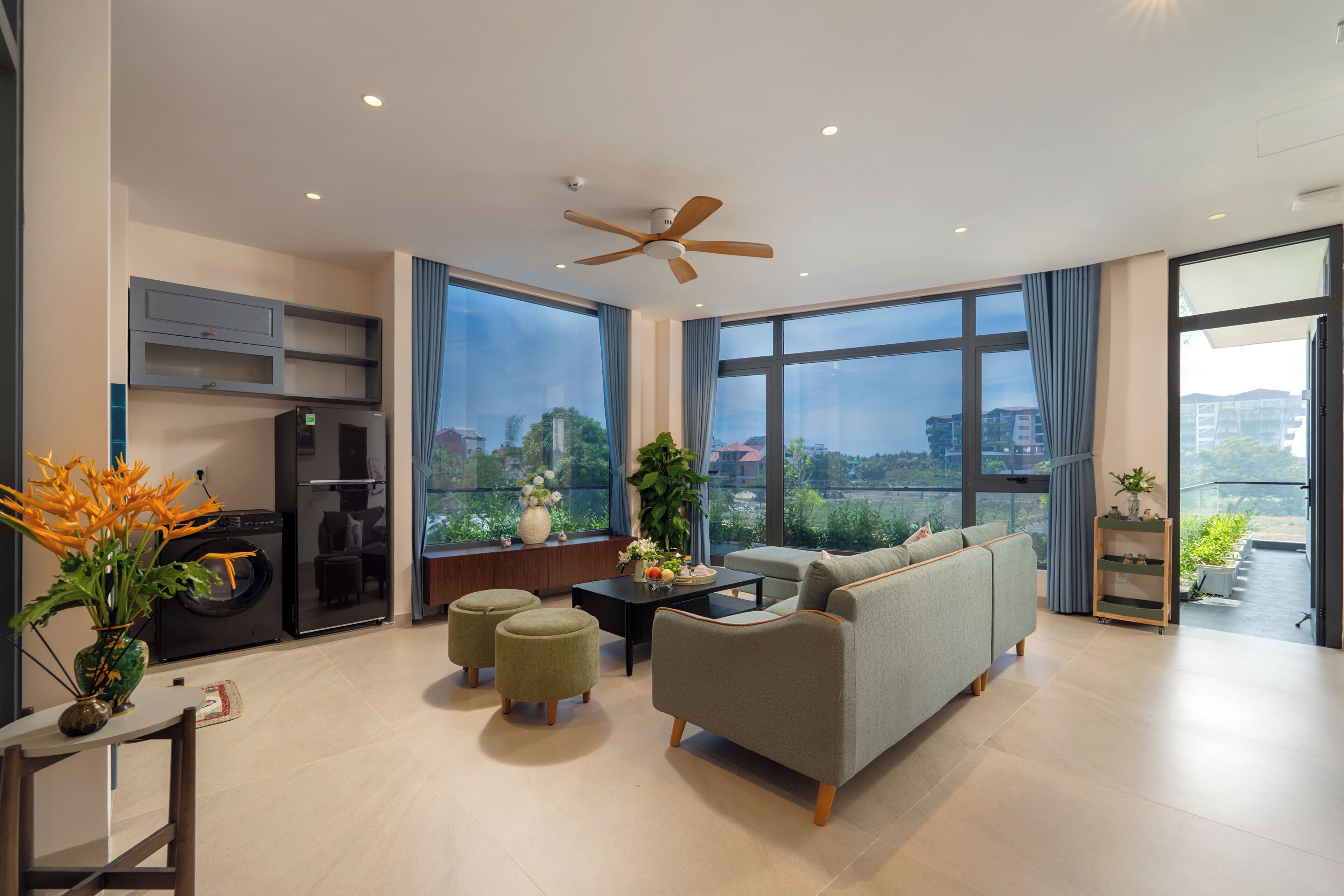 A modern living room with a sofa, ottomans, a coffee table, a ceiling fan, and a view of the city.