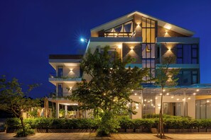A modern multi-story hotel with a balcony, outdoor seating, and well-lit windows. - Bao Anh Villa (Da Nang)