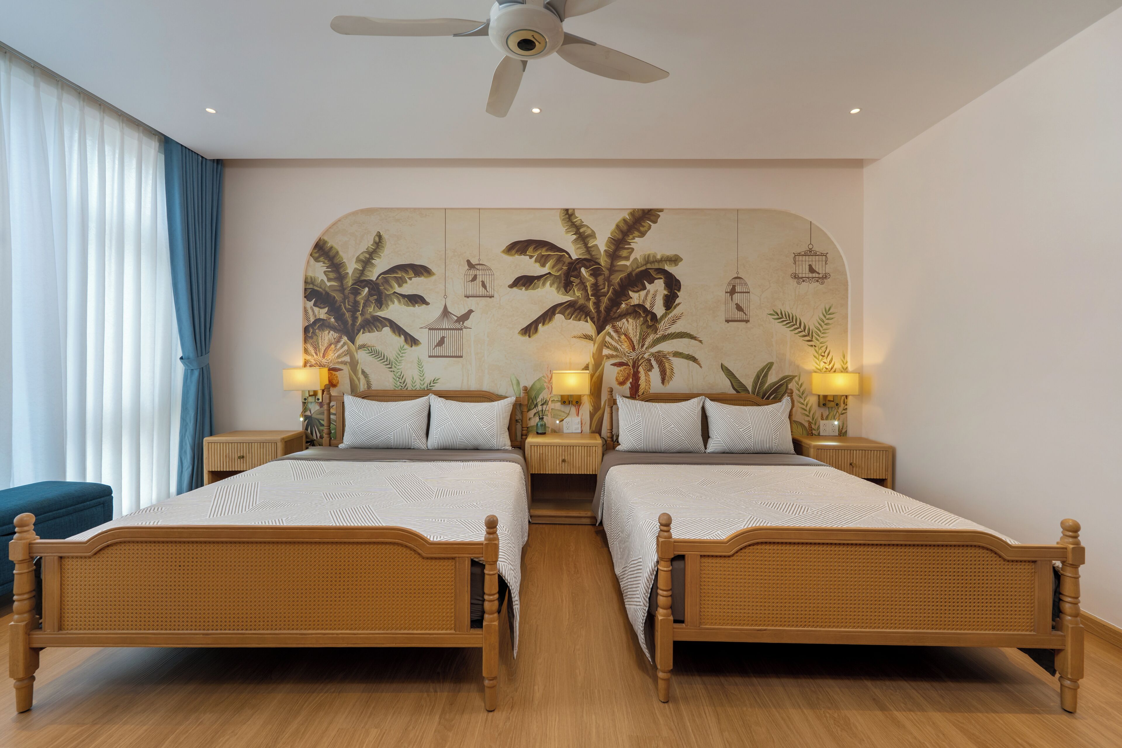 A double bed room with a ceiling fan, two bedside tables with lamps, and a large wall mural with birds and foliage.