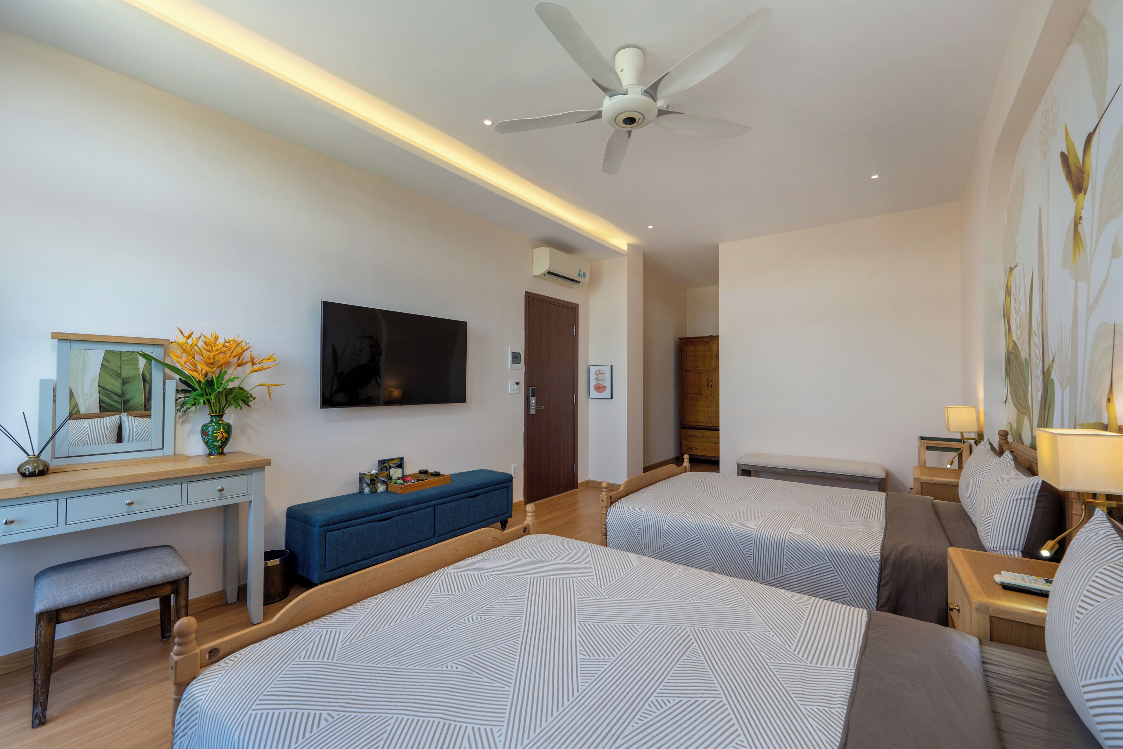 A hotel room with two beds, a desk, a television, and a ceiling fan.