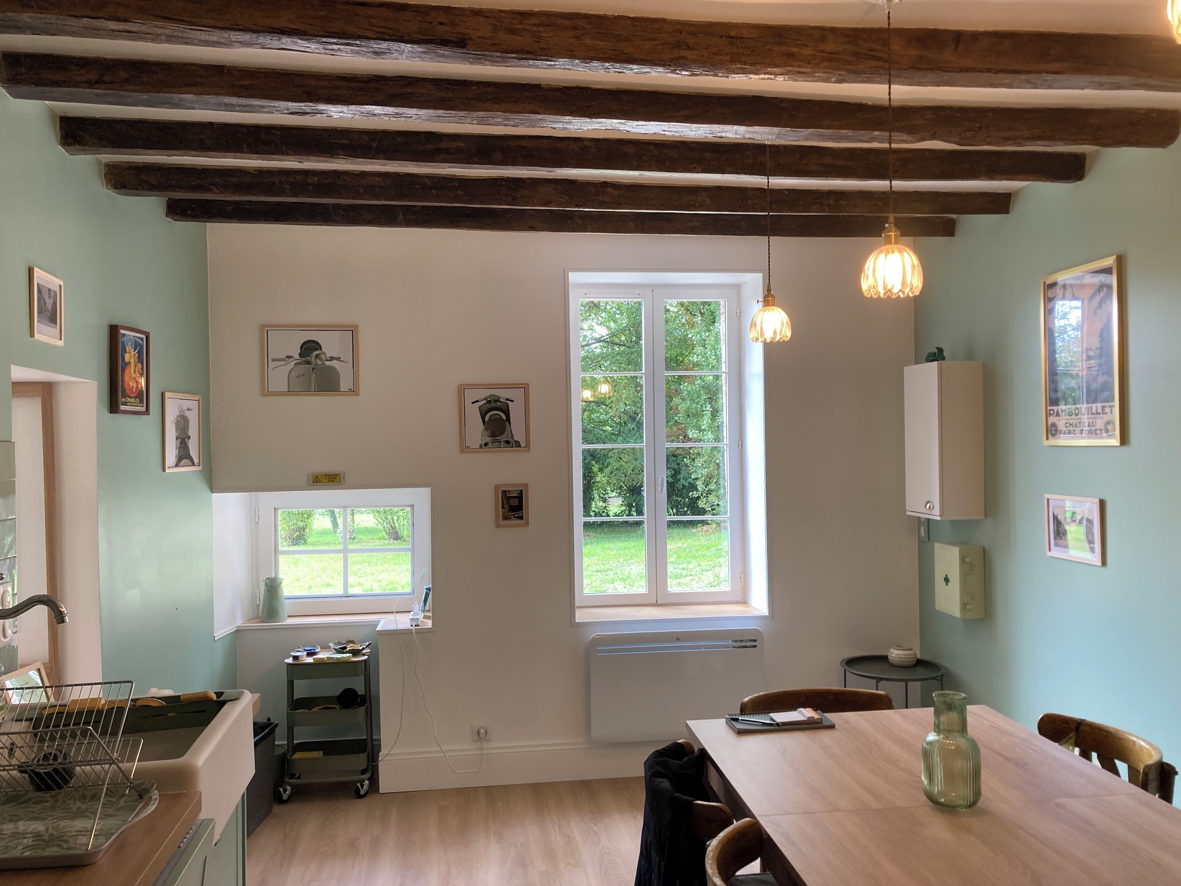 Une cuisine avec une fenêtre, une table à manger et un luminaire suspendu.