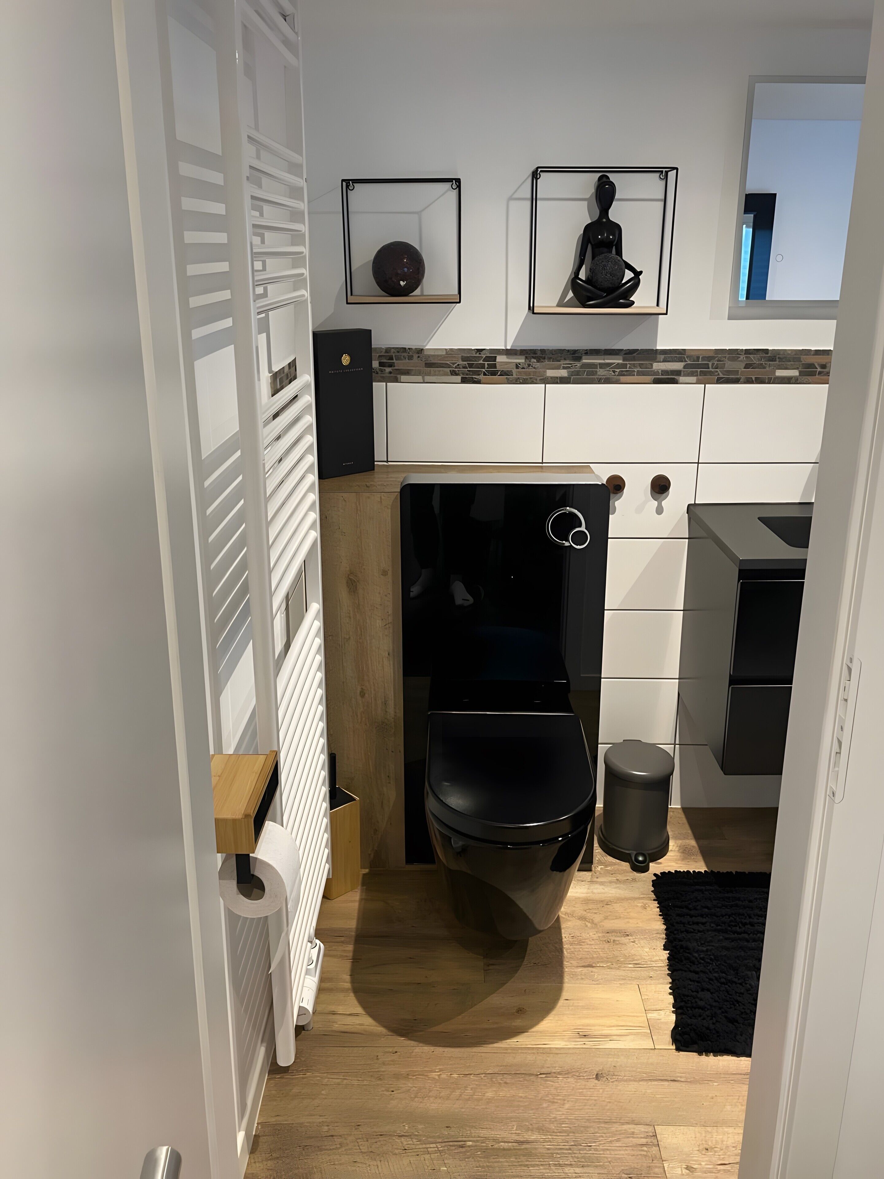 Un baño pequeño con inodoro, un cubo de basura, un estante de madera y un radiador.