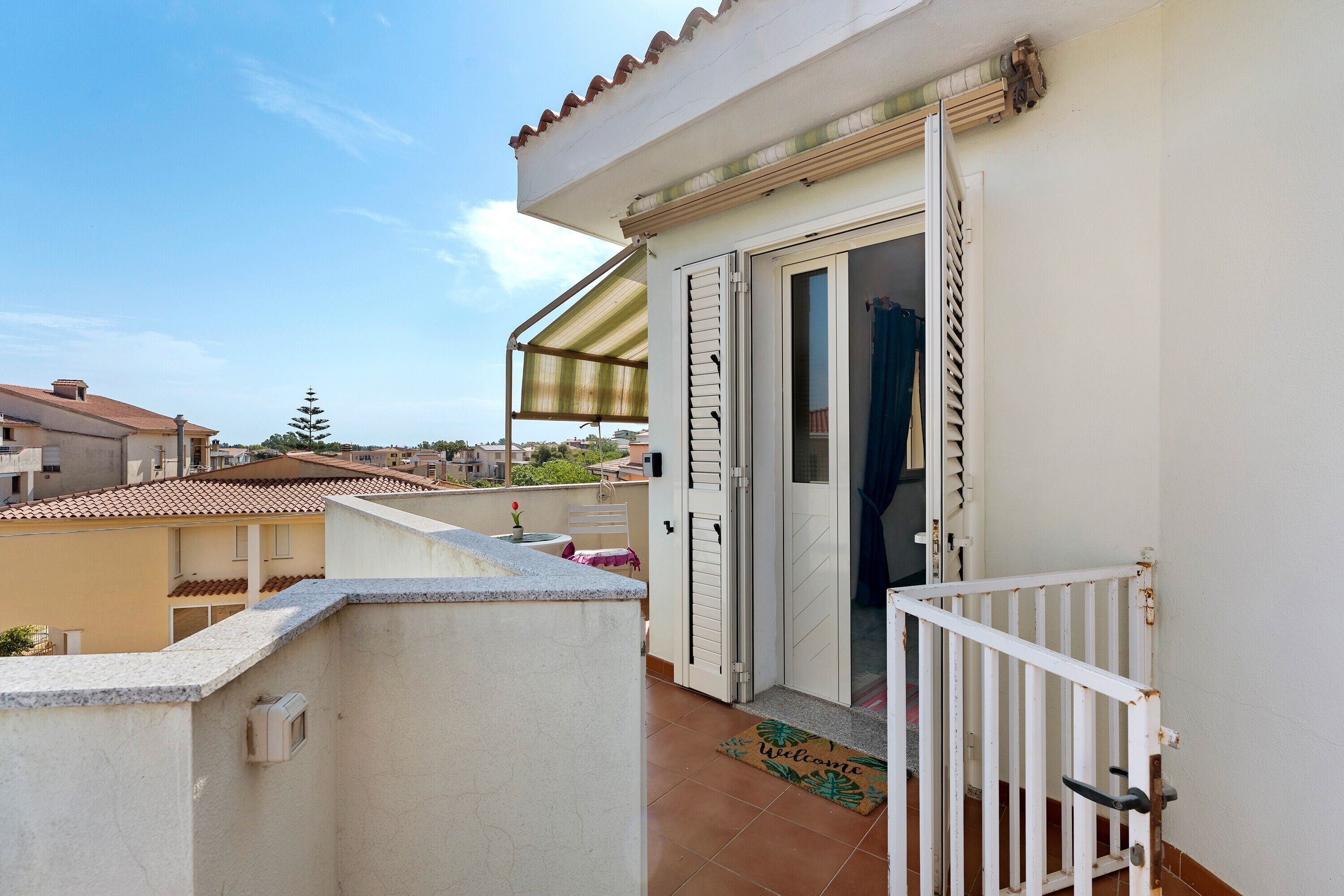 A balcony with a white railing, a door leading to an interior space, and a tiled floor.