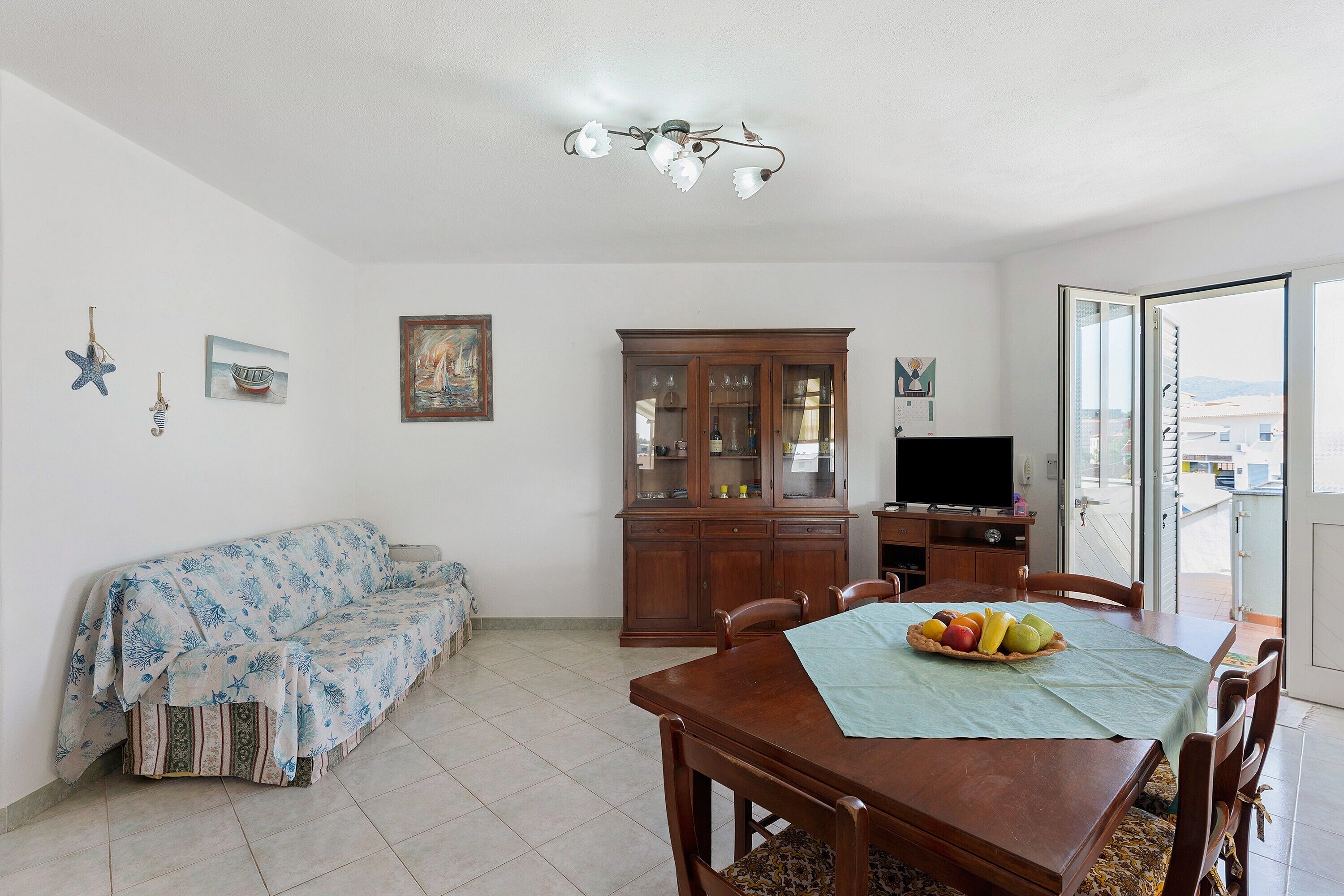 A living room with a sofa, dining table with chairs, a cabinet, and a television.