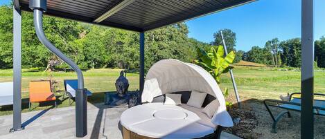 A covered outdoor seating area with a circular sofa and a table, surrounded by a garden and a Buddha statue.
