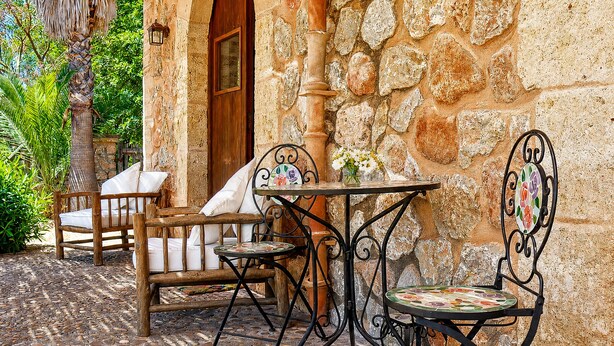 Un muro in pietra, una porta in legno e un patio piastrellato con mobili da esterno.