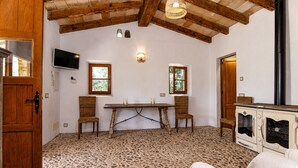 Una stanza con soffitto in legno, pavimento piastrellato, un tavolo con sedie, una televisione e un forno d'epoca.