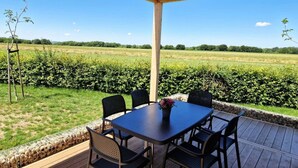 An outdoor patio with a table and chairs, a pergola overhead, and a view of a green field. - Holiday Home With 1 Bedroom (Berg en Terblijt)