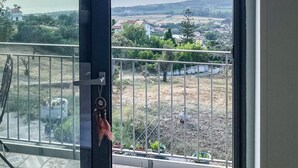 Un balcó amb barana metàl·lica, vista a un paisatge llunyà i una porta que hi dona.