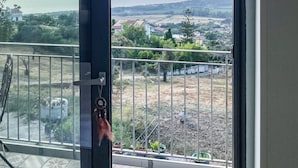 Een balkon met een metalen hekwerk, een uitzicht op een veraf gelegen landschap, en een deur die naar het balkon leidt.