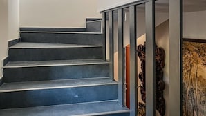 Een trap met donkere treden die naar een tweede verdieping leidt, kunstwerken in de lijsten aan de muren en een glazen balustrade.