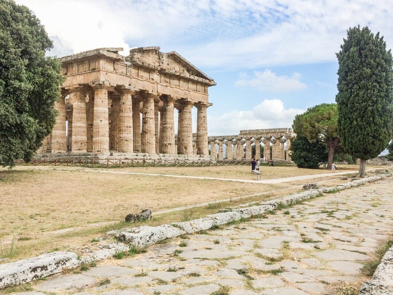 Un ancien temple grec, avec ses colonnes, un chemin pavé et un ciel dégagé.
