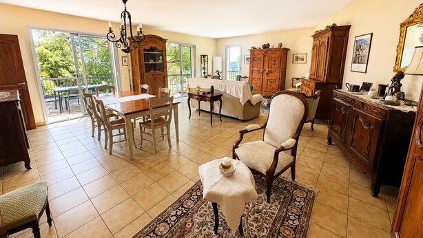 A spacious living area with a dining table, chairs, a sofa, a patterned rug, and a large window offering a view of greenery. - La Musardière - Air Conditioning, Pool with a View - Sleeps 8 (Villeneuve-lès-Avignon)