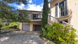 A two-story building with a stone-paved courtyard, a balcony with a car parked outside, and a tall tree in the center. - La Musardière - Air Conditioning, Pool with a View - Sleeps 8 (Villeneuve-lès-Avignon)