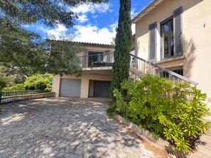 A two-story building with a stone-paved courtyard, a balcony with a car parked outside, and a tall tree in the center. - La Musardière - Air Conditioning, Pool with a View - Sleeps 8 (Villeneuve-lès-Avignon)