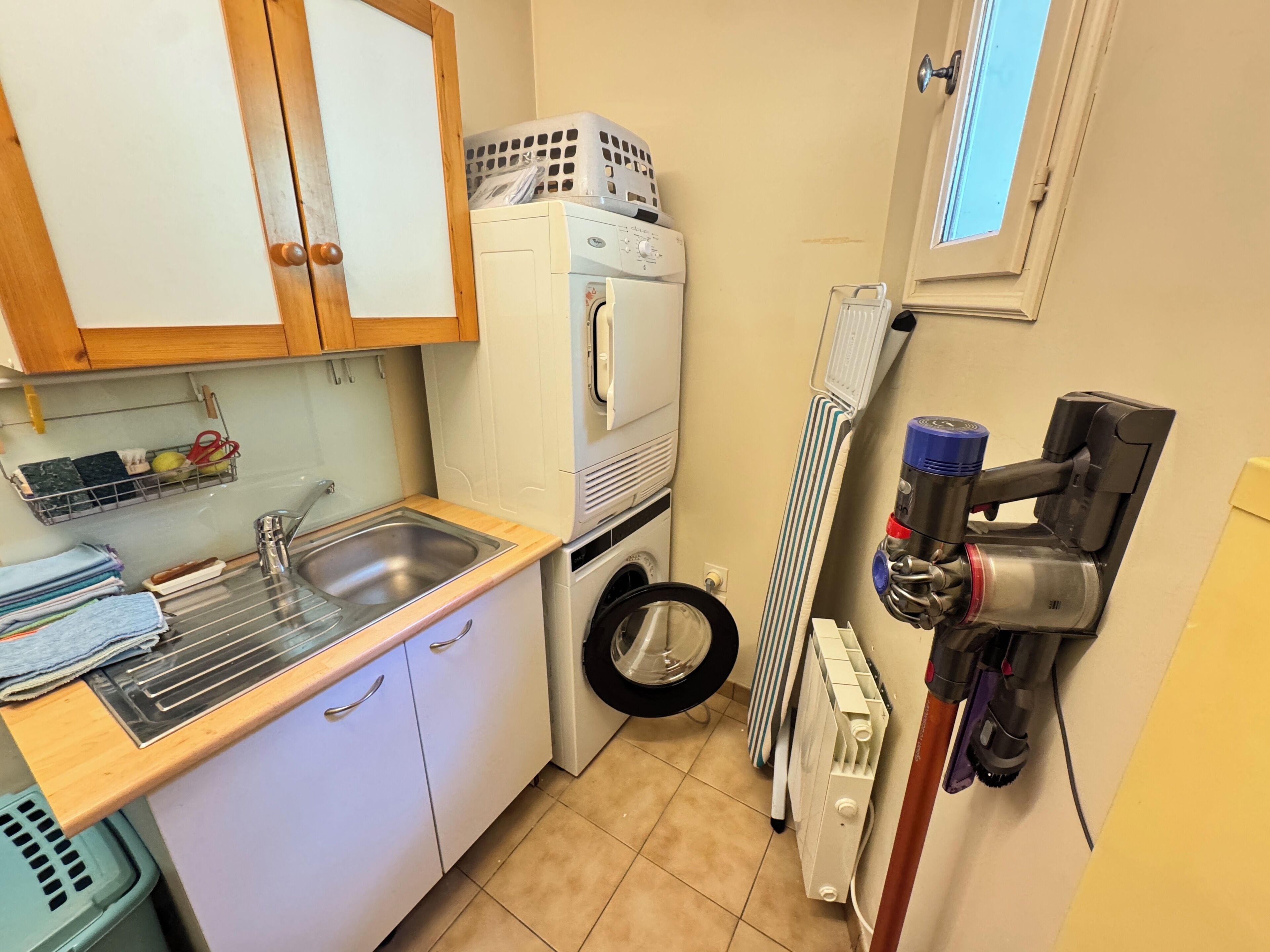 A compact kitchen with a sink, a washing machine, a radiator, and a vacuum cleaner.
