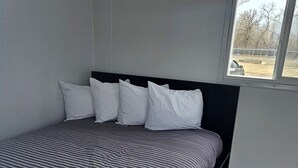 Une chambre à coucher avec un lit, des oreillers, une fenêtre et une vue sur l’extérieur.