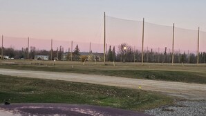 Un terrain de sport entouré d’une clôture, avec une route et des bâtiments en arrière-plan.