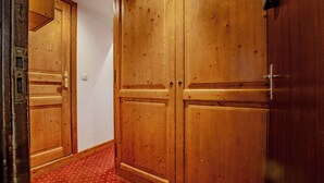 Un pasillo con puertas dobles de madera, alfombra roja estampada y una lámpara en el techo.