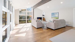 Una sala de estar moderna con chimenea, ventanas amplias y vistas al exterior.