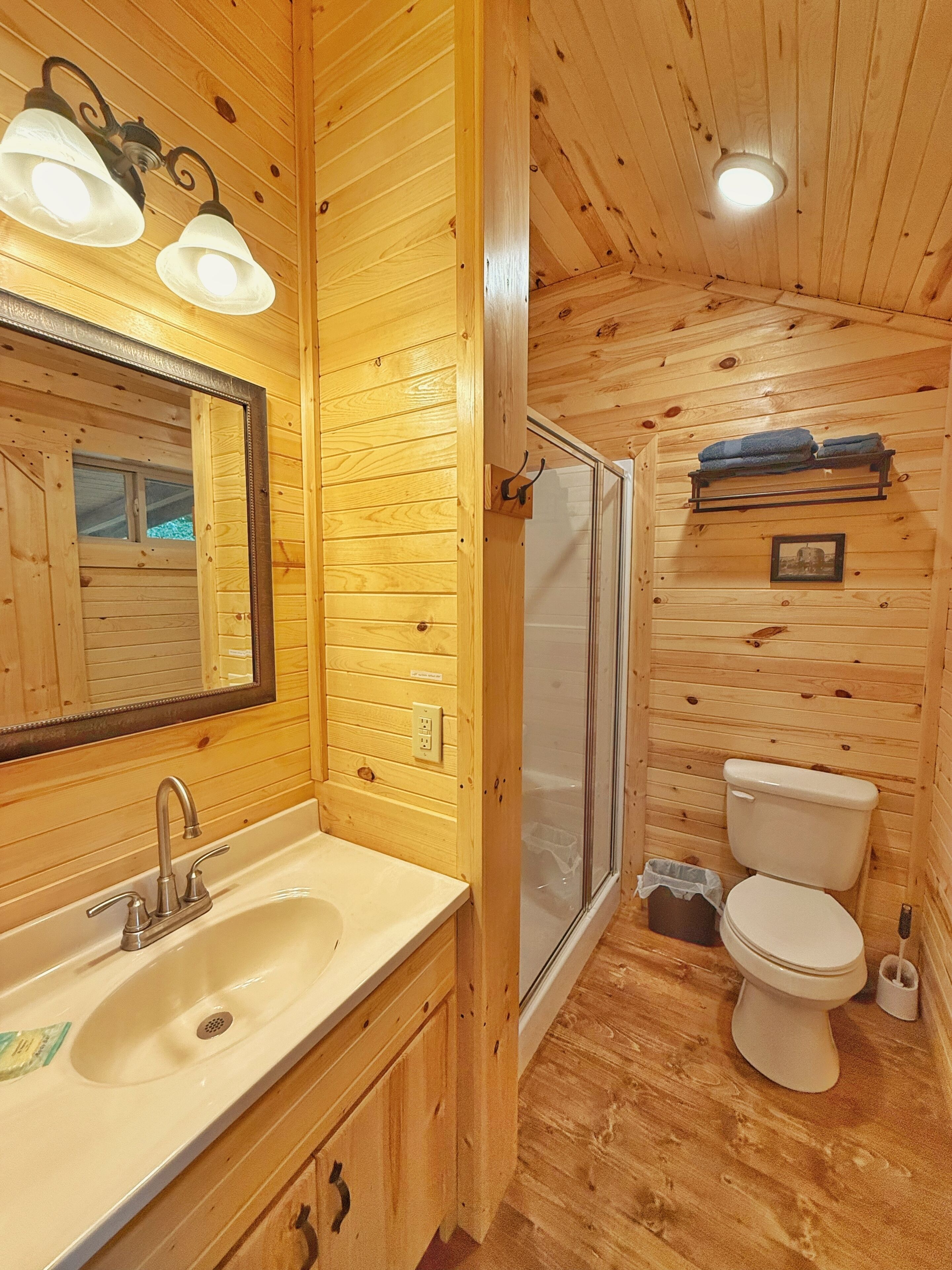 A wooden cabin bathroom with a sink, mirror, shower, and toilet.