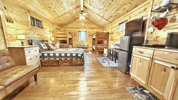 Une cabane en rondins avec un intérieur en bois, un lit superposé, une kitchenette et un coin repas.