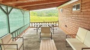 Un espace extérieur abrité avec des bancs en bois et des tables de pique-nique, offrant une vue sur un champ verdoyant, et une structure en bois qui ressemble à un chalet.