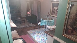 Ein Zimmer mit Esstisch, Stühlen, einem kleinen runden Tisch mit Lampe, einer Couch, einem gemusterten Teppich und einem Bild an der Wand.