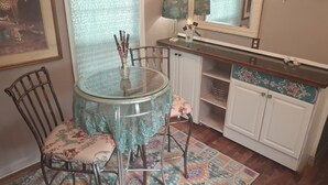 Ein Essbereich mit einem Glastisch, floralen Stühlen, einem gemusterten Teppich, einem Schrank mit floraler Verzierung und einem Spiegel über der Arbeitsplatte.