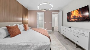 A modern bedroom with a large bed, a television displaying a fire, a walk-in closet, and a bathroom visible through an open door. - 6BR house sleeps 16 with private pool (Kissimmee)
