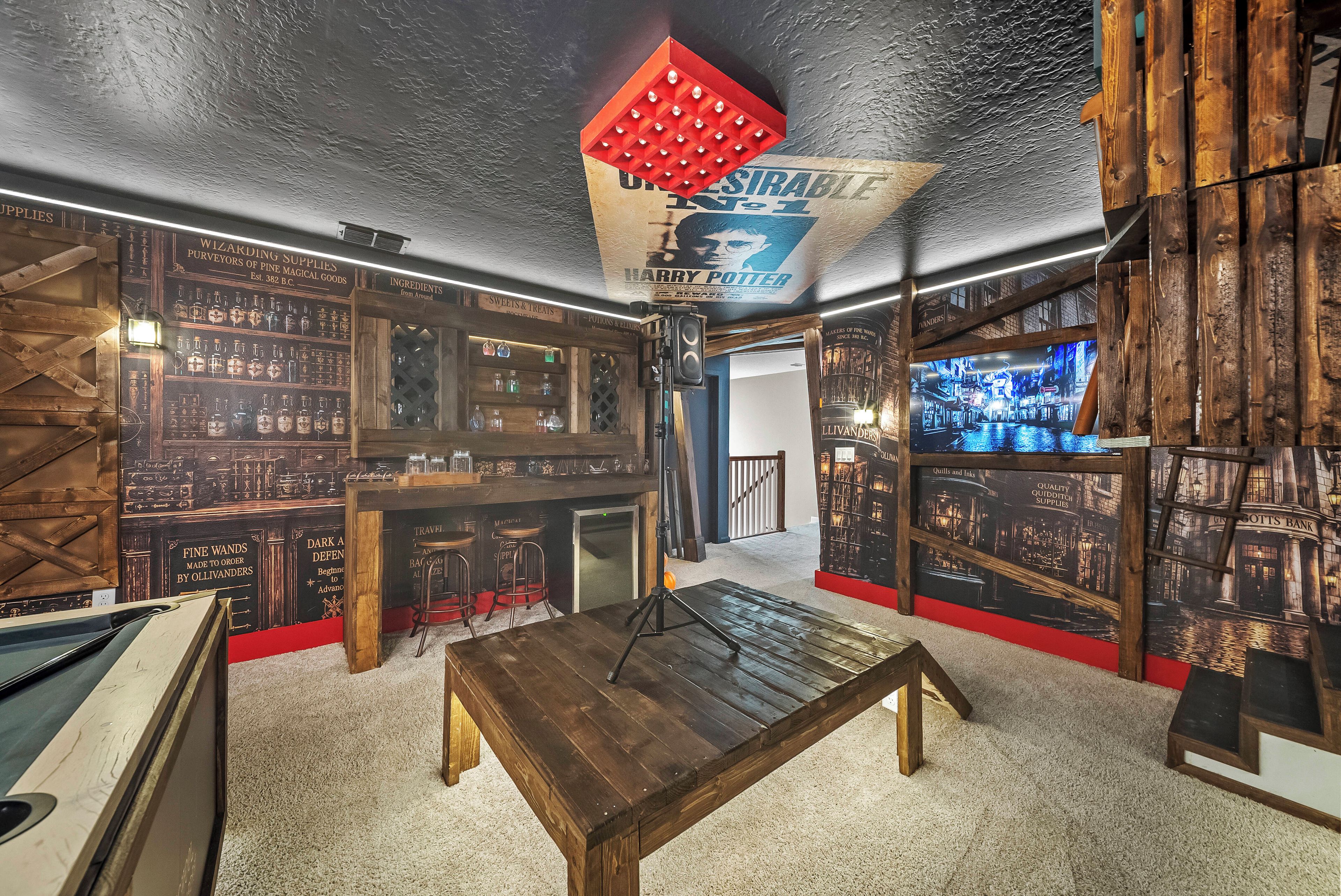 Een kamer met een houten tafel, planken met glaswerk en een muur in Harry Potter-thema.
