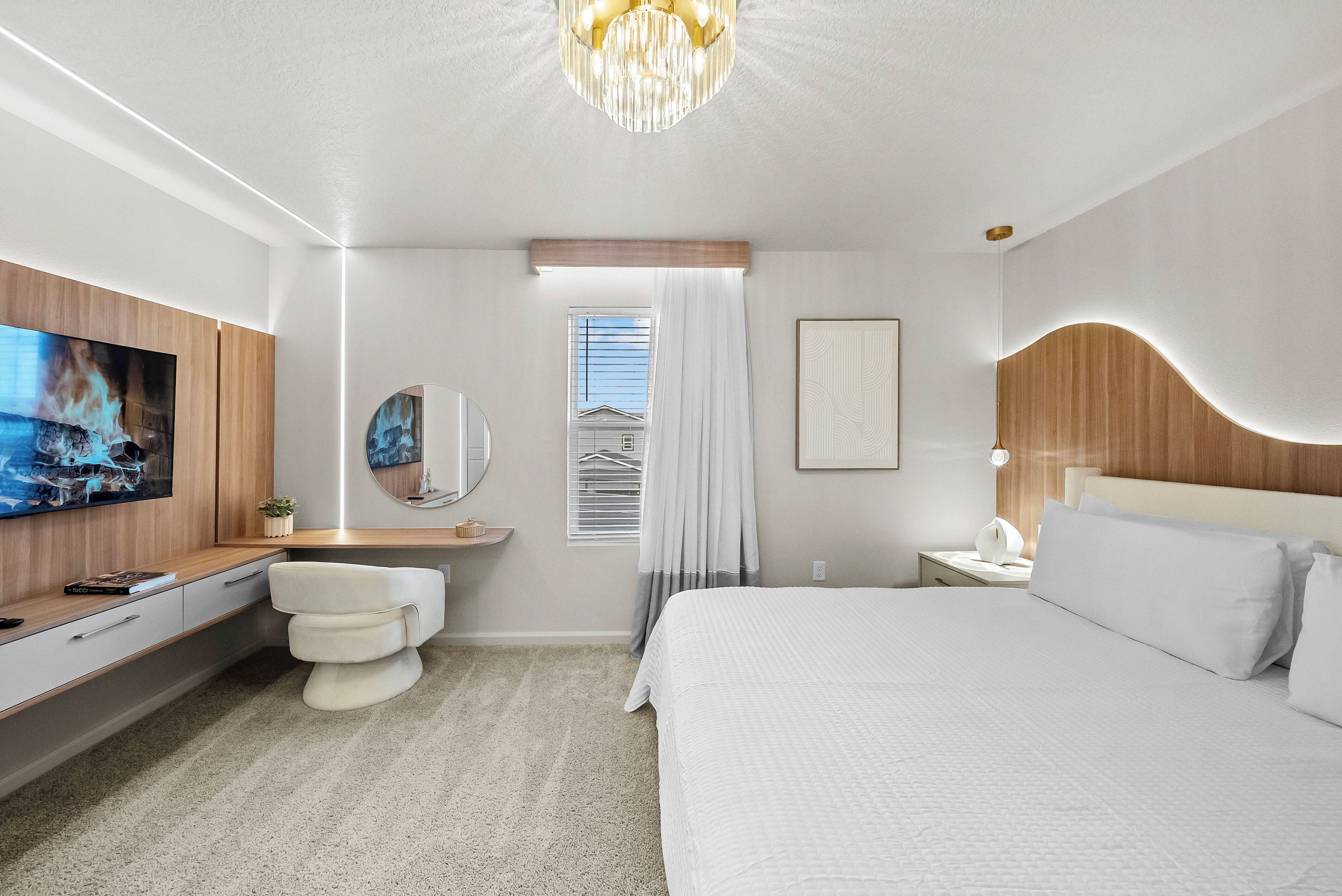Une chambre d’hôtel moderne avec un grand lit, un téléviseur fixé au mur, une table de chevet, un miroir et une fenêtre avec des rideaux.