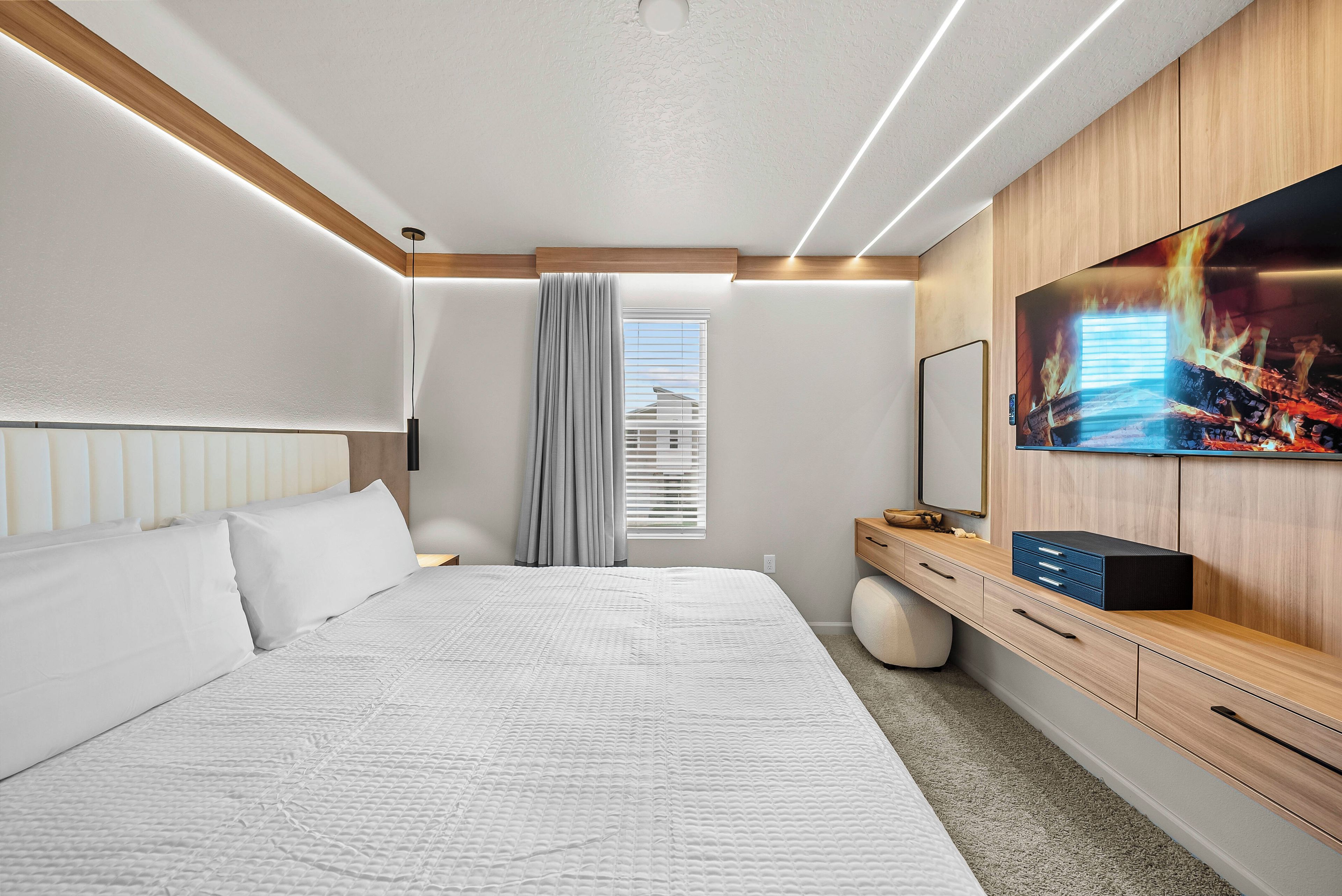 Ein modernes Hotelzimmer mit einem großen Bett, einem Flachbildfernseher, einer hölzernen Kommode und einem Fenster mit Jalousien.