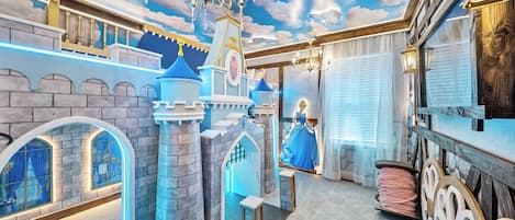 A room with a castle-themed design, including a chandelier, a large window with curtains, and a decorative wall.