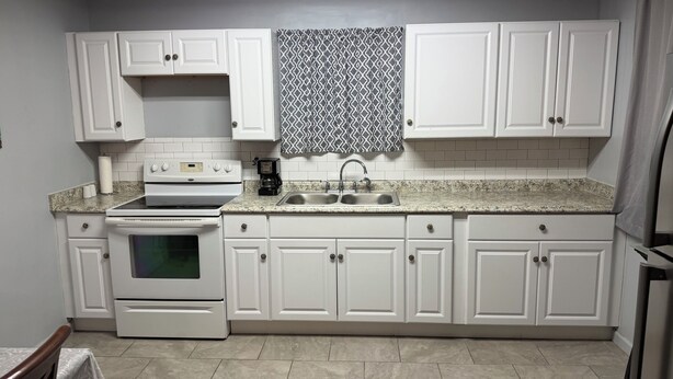 A kitchen with white cabinets, a stove, a sink, and a patterned window treatment.