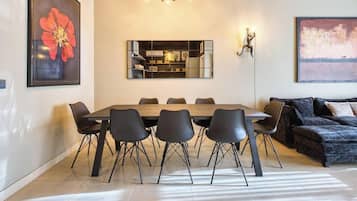 Un comedor con una mesa rectangular, seis sillas, un sofá, un espejo en la pared y dos obras de arte.