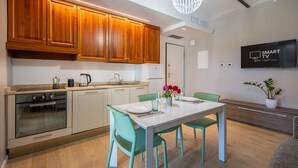 A modern kitchen with wooden cabinets, a built-in oven, and a dining area with a white table and teal chairs. - Alba Palace Luxury Apartments - White (Alba)