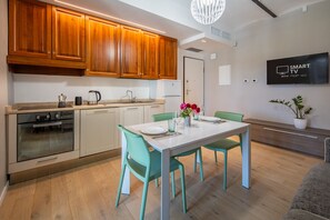 Eine moderne Küche mit Holzschränken, einem eingebauten Ofen und einem Essbereich mit weißem Tisch und türkisfarbenen Stühlen.