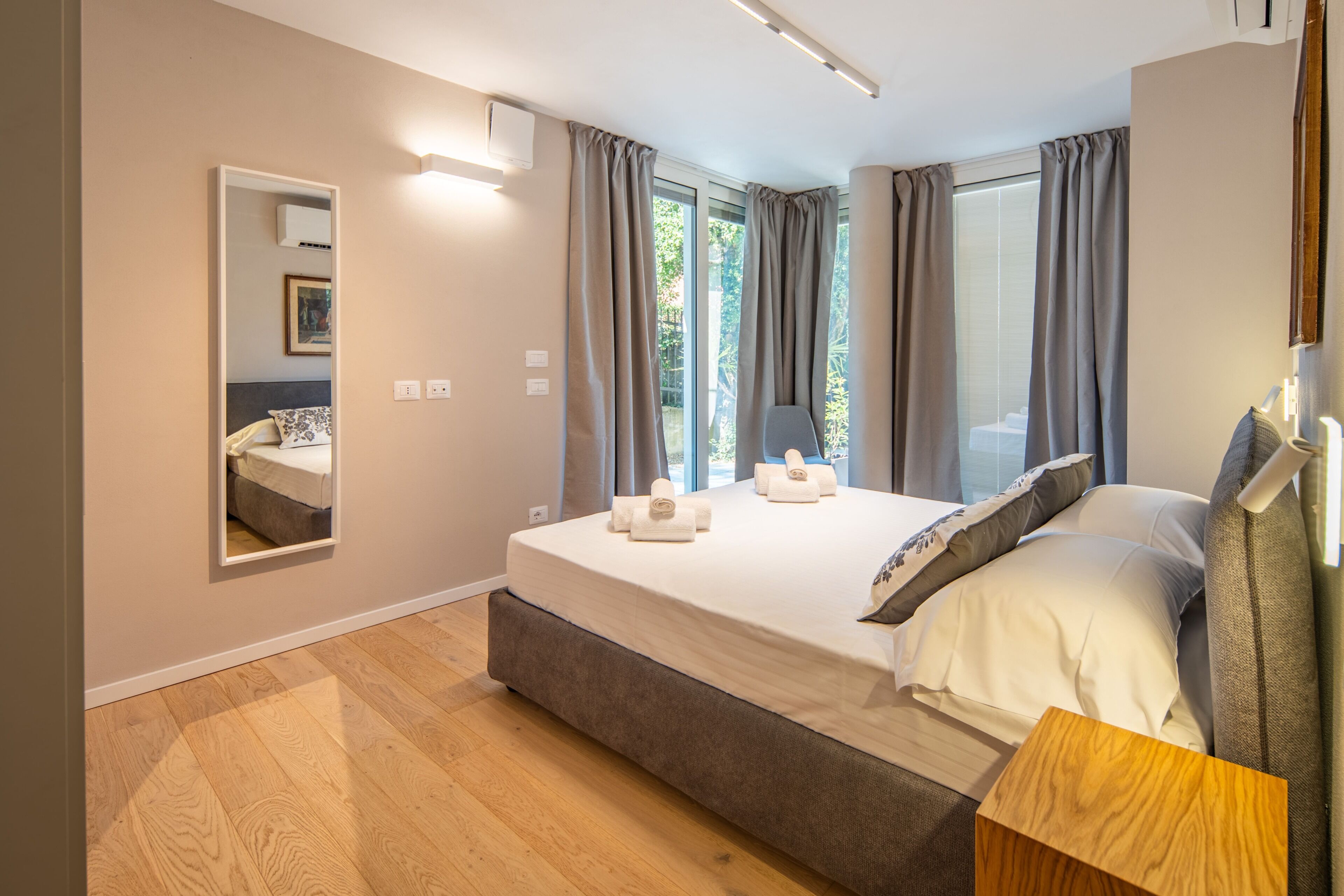 Ein modernes Schlafzimmer mit einem großen Bett, einem Nachttisch, einem Spiegel und einem Fenster mit Vorhängen.
