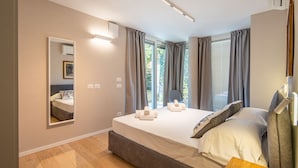 A modern bedroom with a large bed, a bedside table, a mirror, and a window with curtains. - Alba Palace Luxury Apartments - White (Alba)