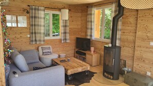 L’intérieur chaleureux d’un chalet avec un canapé, un téléviseur, une table en bois et un poêle à bois.