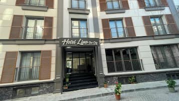 A hotel with a sign reading 'Hotel Lina Old City.' It features multiple balconies with wooden shutters, a stone facade, and a paved entrance area with potted plants.